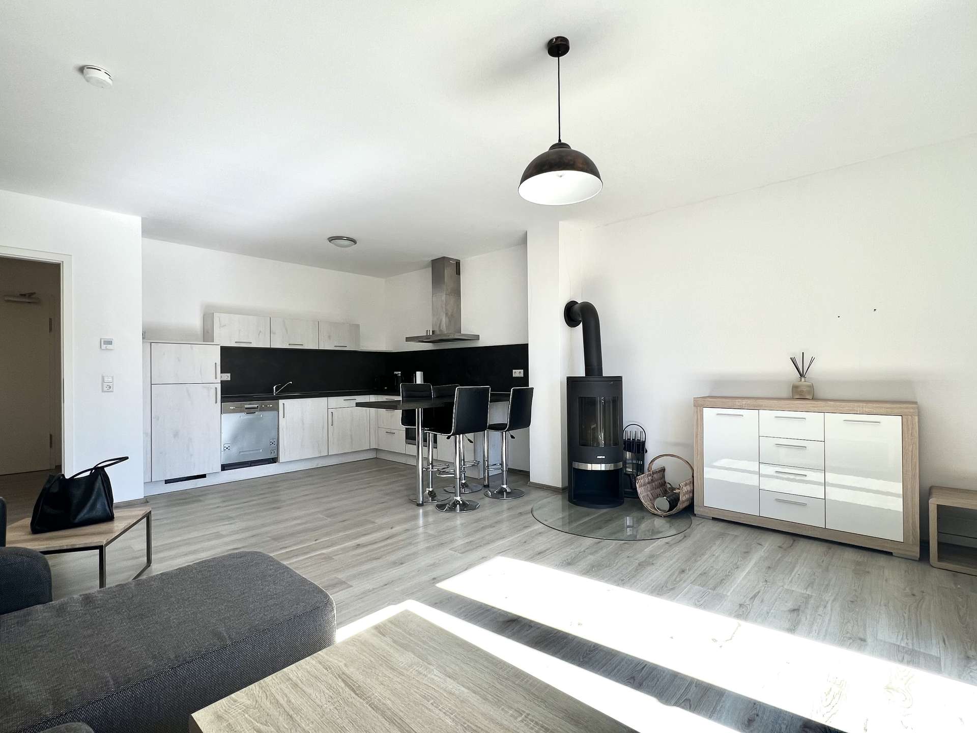 Open-plan kitchen and living area with white cabinets, black backsplash, and a central island with chrome bar stools.