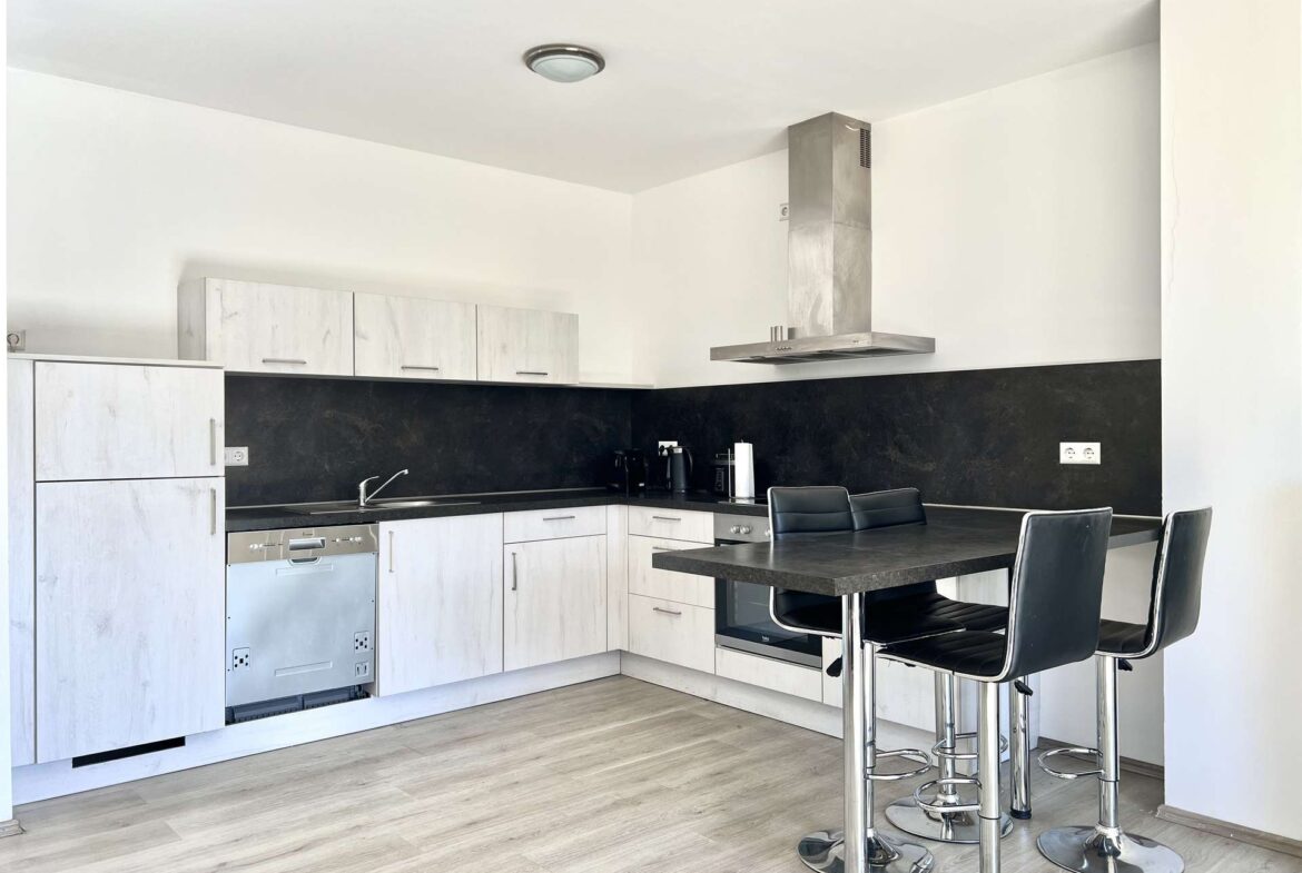 Modern L-shaped kitchen with white cabinets, black backsplash, stainless appliances, and a tall island with chrome bar stools.