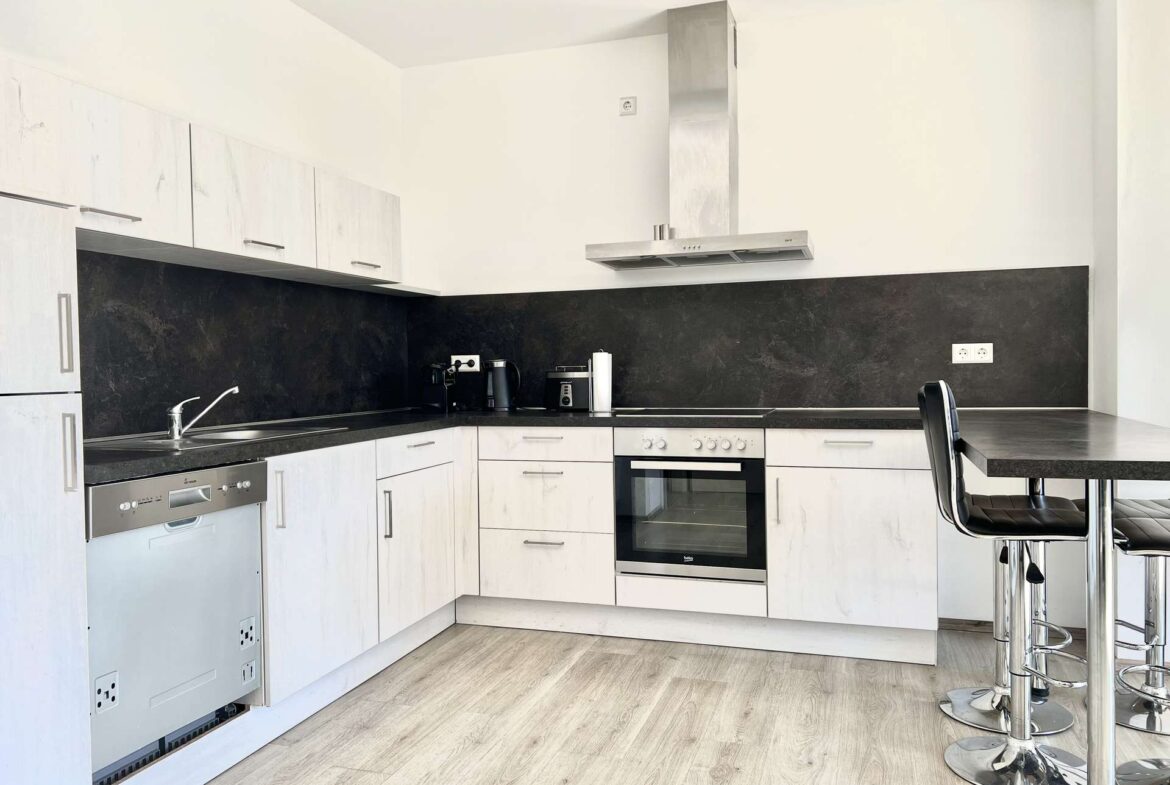 Modern L-shaped kitchen with white cabinets, black countertops, and a stainless steel oven and range hood.