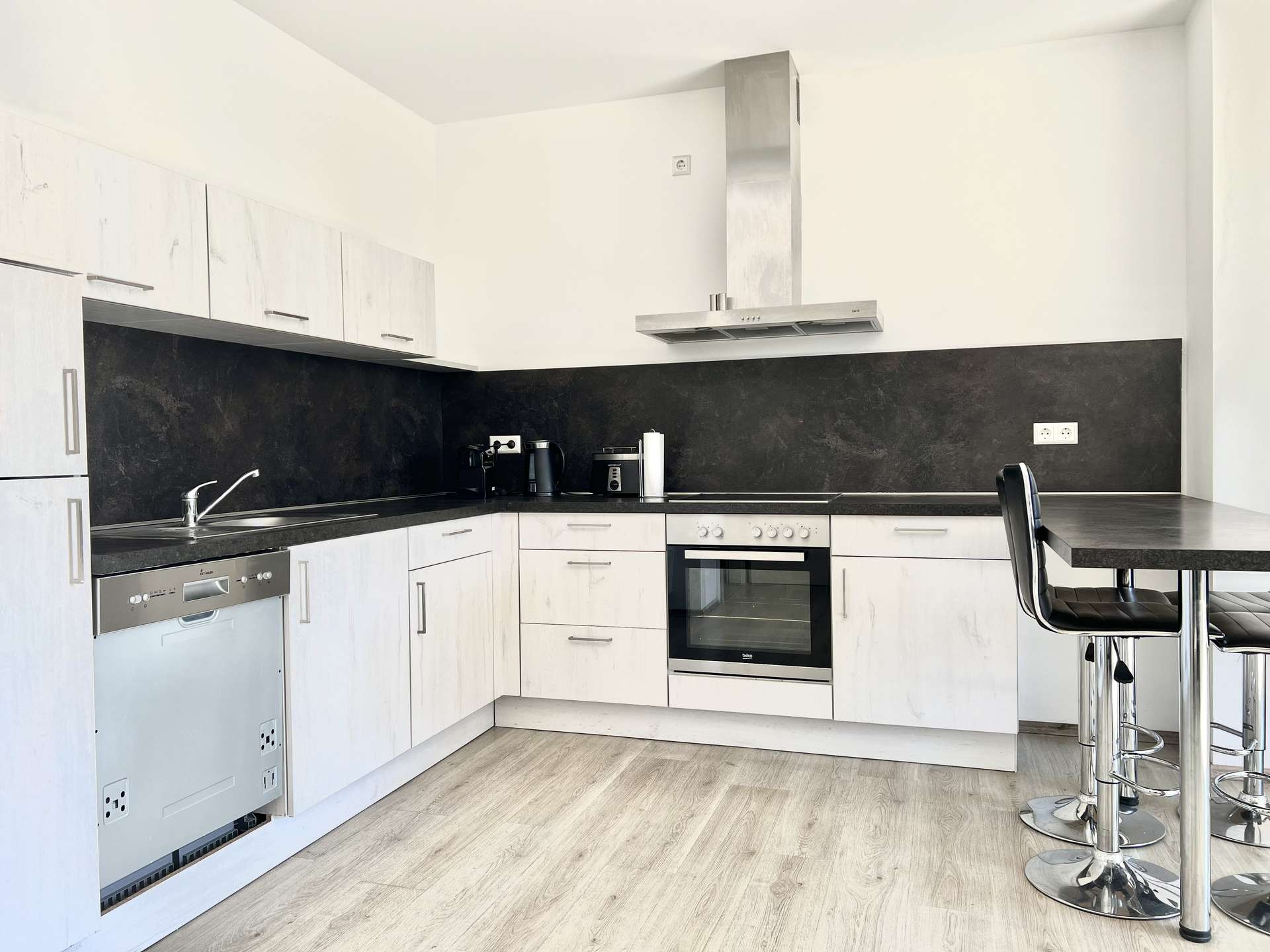 Modern L-shaped kitchen with white cabinets, black countertops, and a stainless steel oven and range hood.