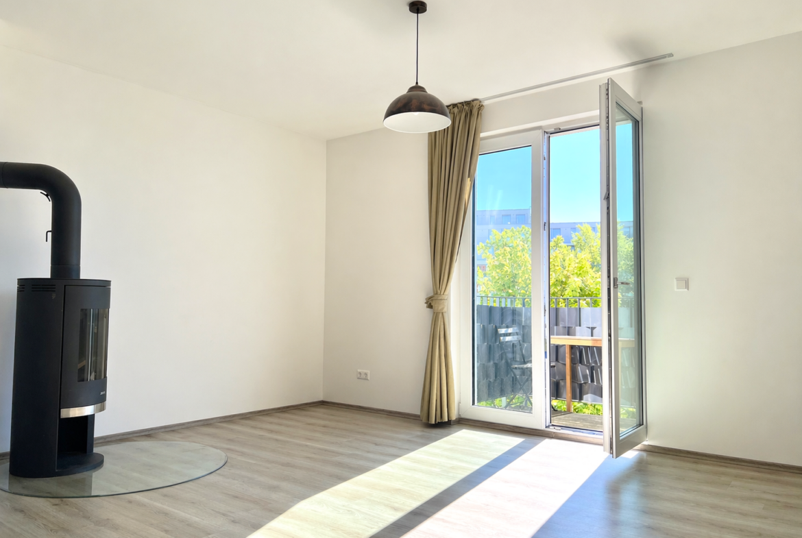 Bright, minimalist living room with a black modern stove on the left, and an open glass door to a sunny balcony outside.