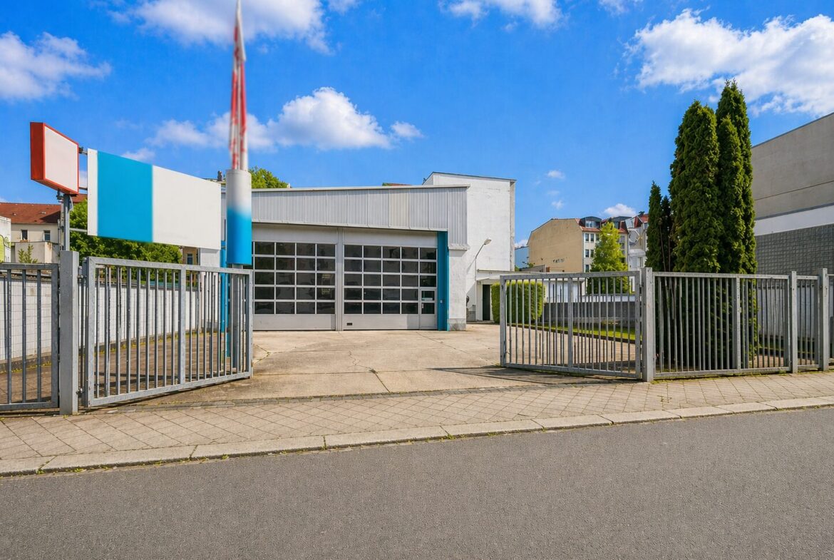 Gate-accessed auto repair or service station with a large glass-pane garage door and blue-white façade under a bright blue sky.