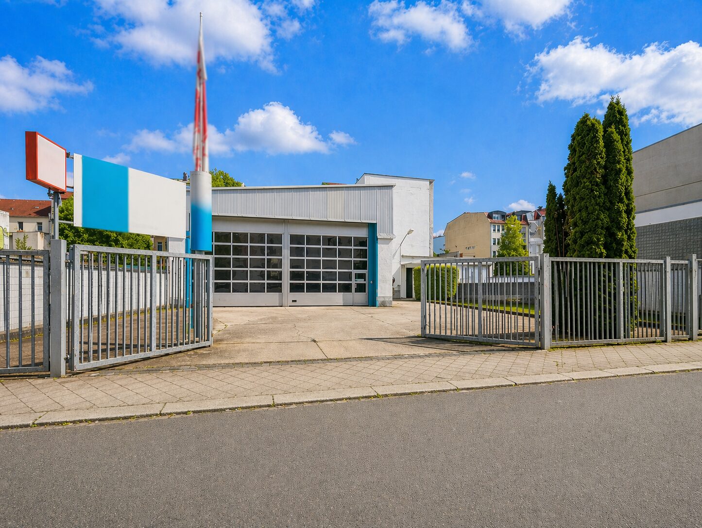 Gate-accessed auto repair or service station with a large glass-pane garage door and blue-white façade under a bright blue sky.