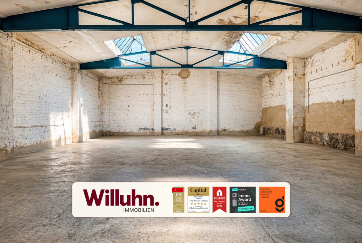 Empty industrial warehouse interior with white brick walls, blue steel trusses, and skylights; a Willuhn Immobilien banner along the floor.