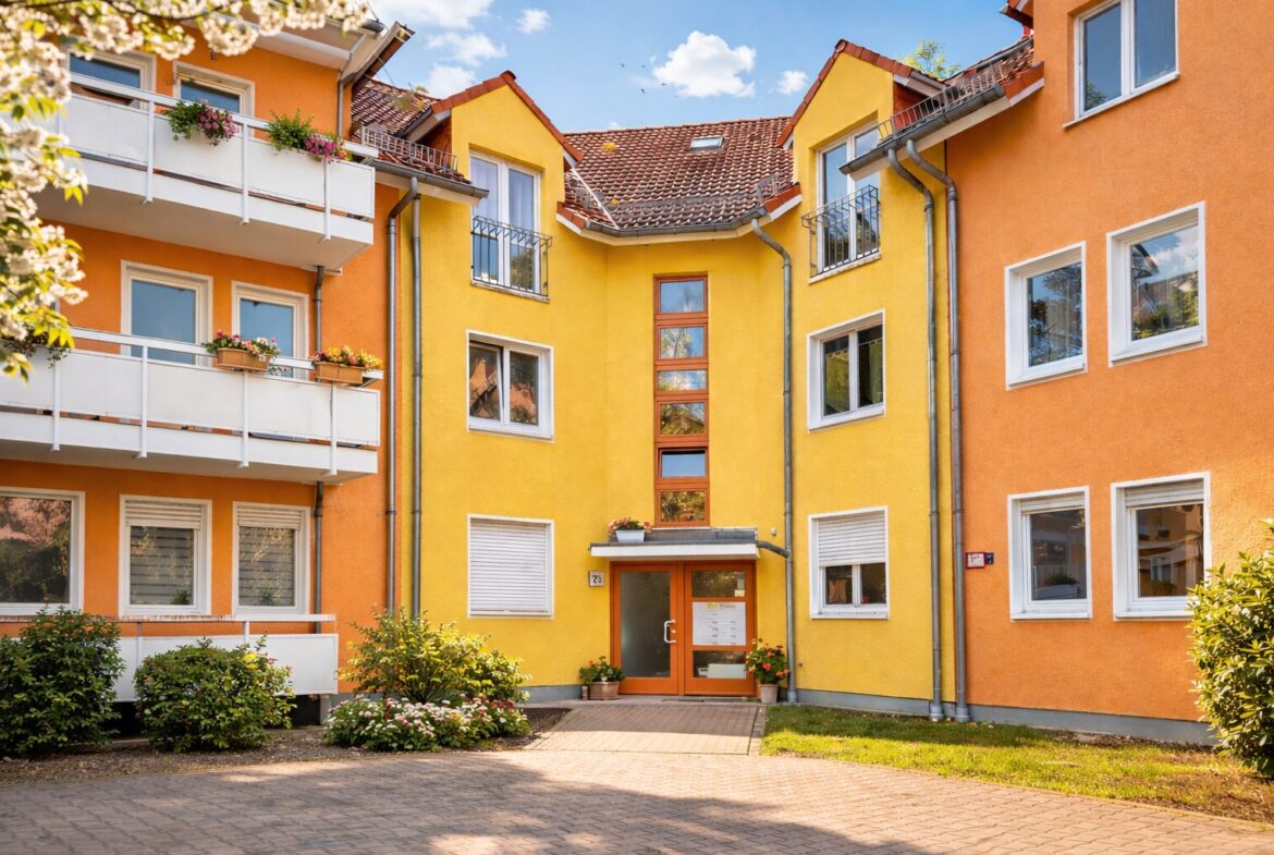Colorful apartment building courtyard with orange and yellow facades, balconies with flowers, and a central entry door.
