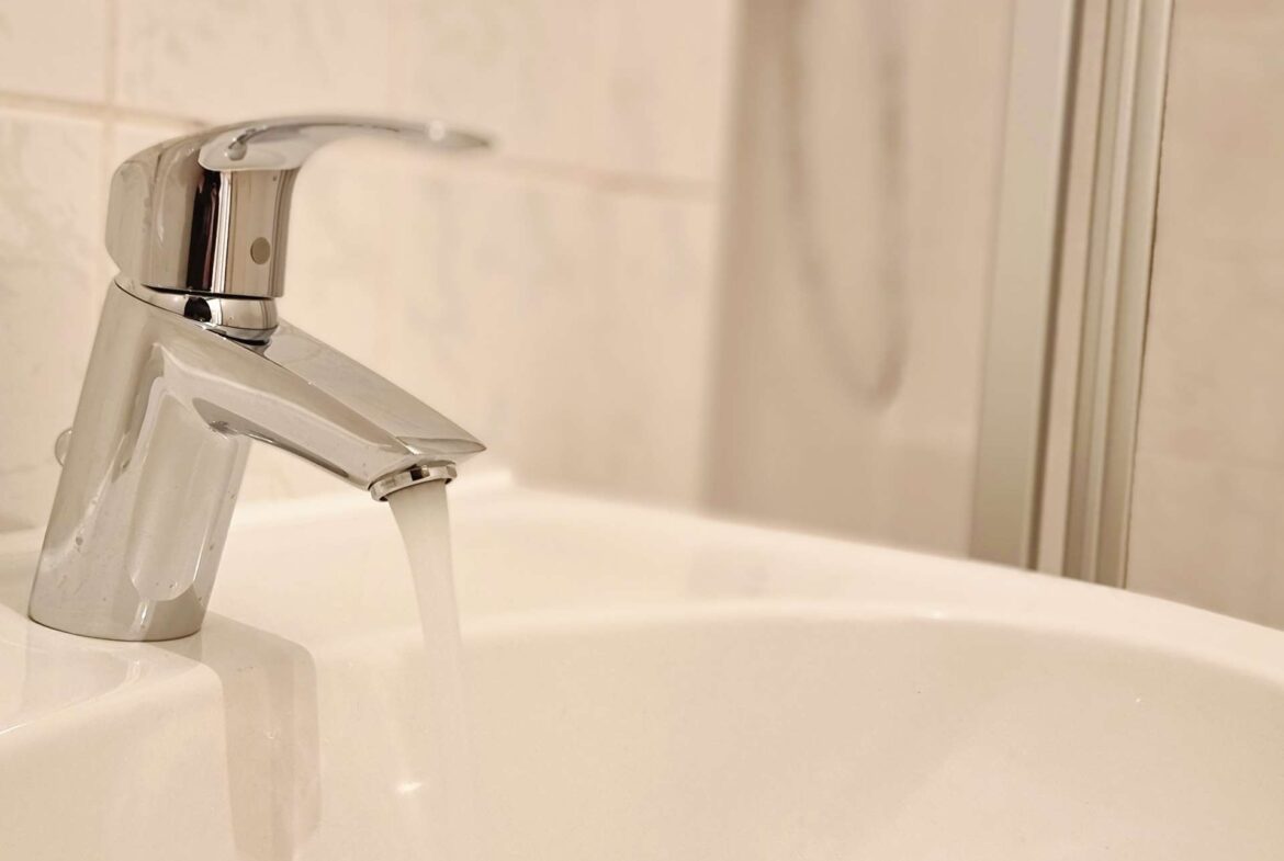Close-up of a chrome bathroom faucet with water flowing into a white sink