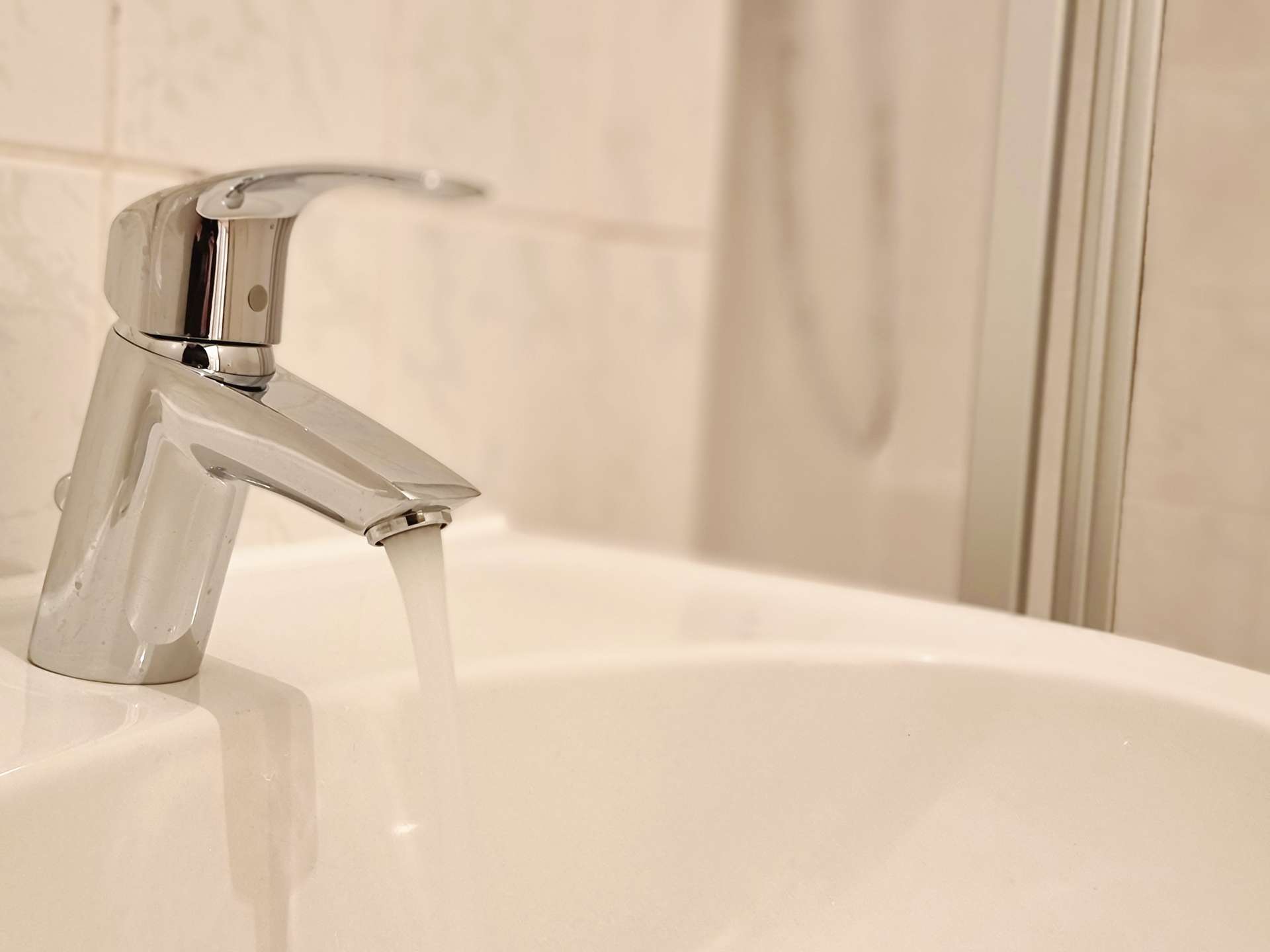 Close-up of a chrome bathroom faucet with water flowing into a white sink