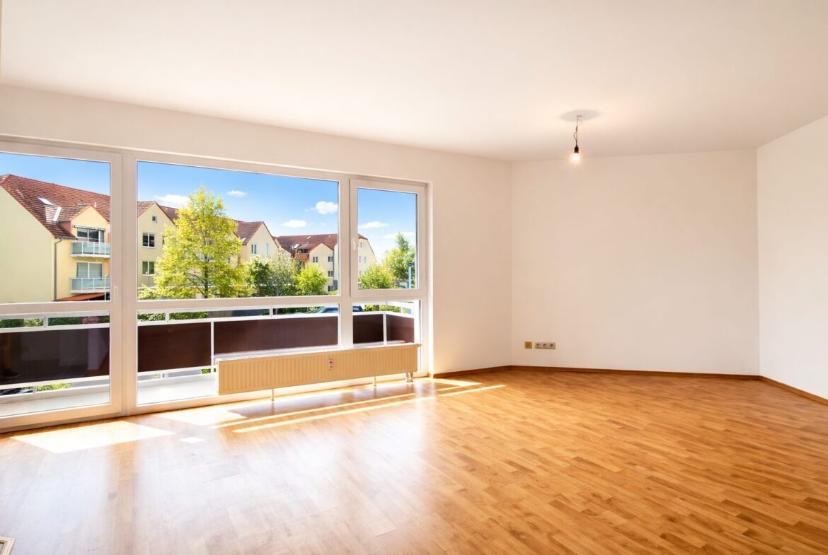 Bright empty living room with large floor-to-ceiling windows and a wooden floor.