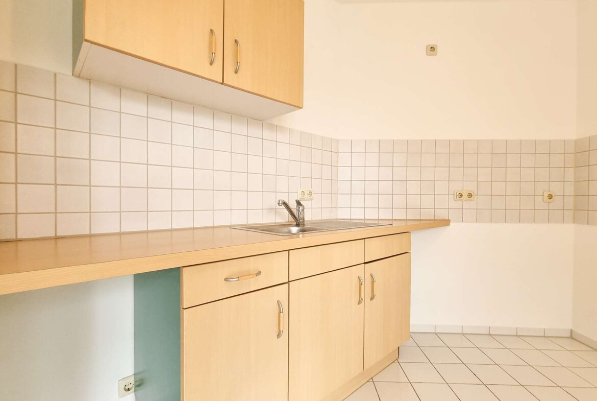 Bright kitchen with light wood upper and lower cabinets, white tiled backsplash, and a stainless steel sink. (Informative)