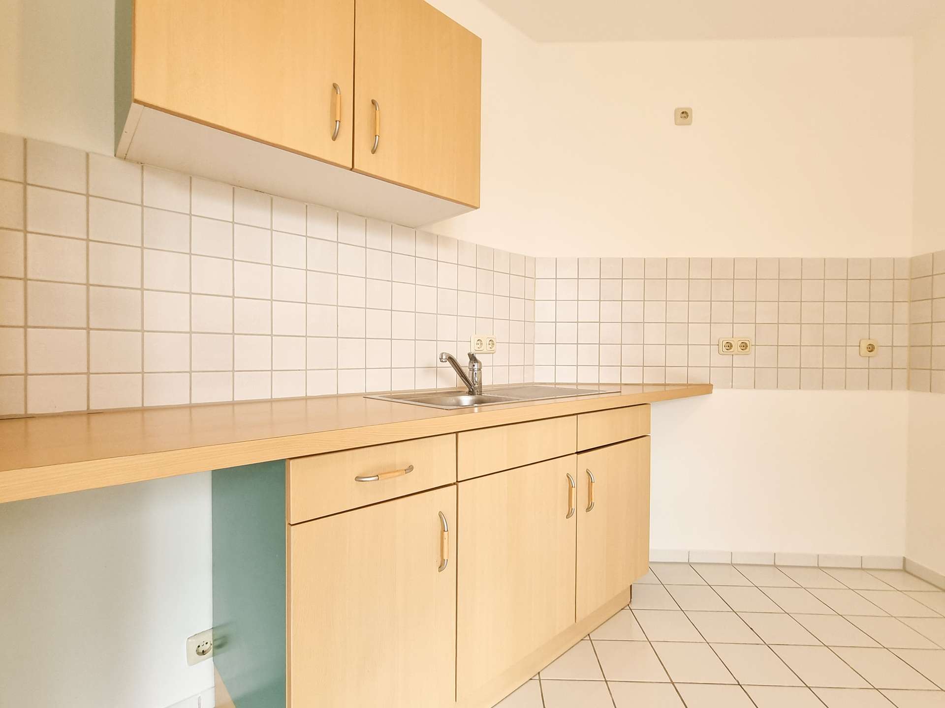 Bright kitchen with light wood upper and lower cabinets, white tiled backsplash, and a stainless steel sink. (Informative)