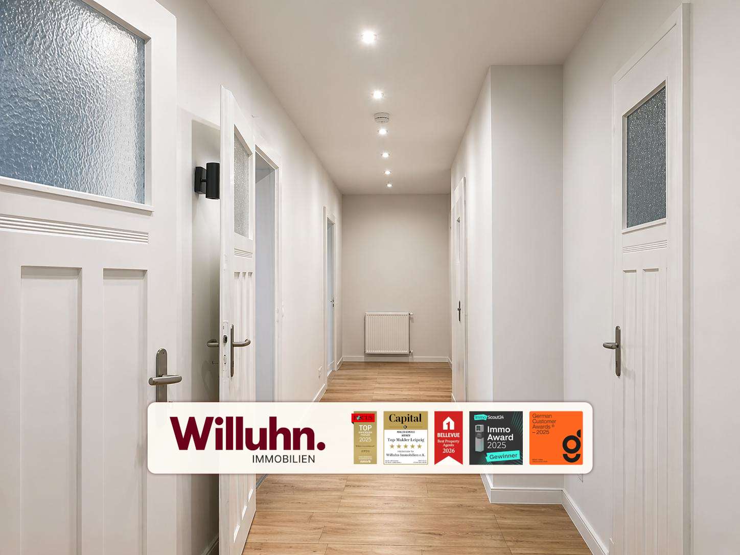 Bright hallway with white doors, light wood floor, and recessed ceiling lights; radiator at the far end.