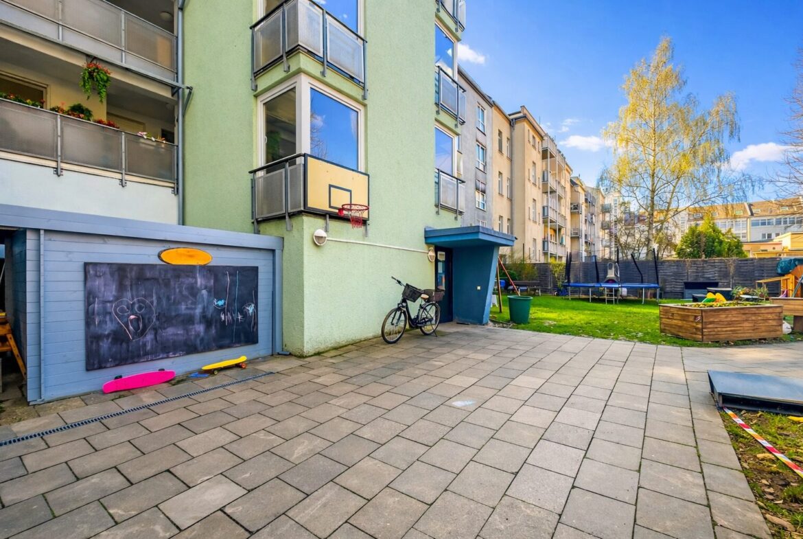 Courtyard of a residential building with a blue shed displaying chalk drawings, a bicycle parked nearby, and colorful skateboards on the ground.