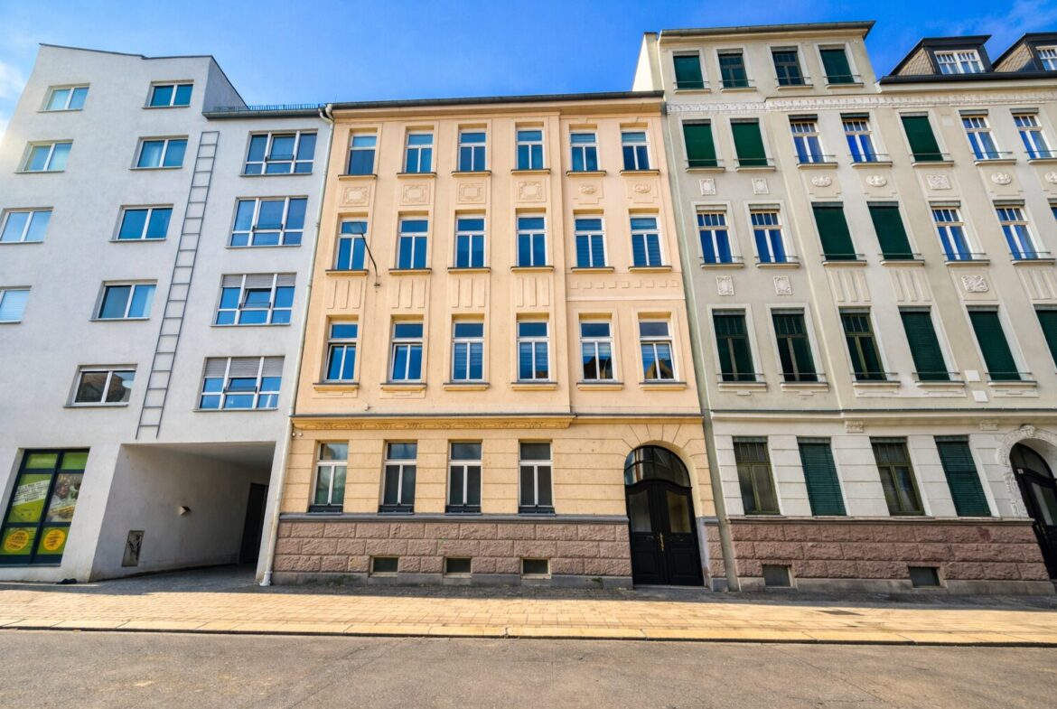 Row of pastel-colored, multi-story buildings with decorative facades along a sunny street and a dark arched doorway in the center building