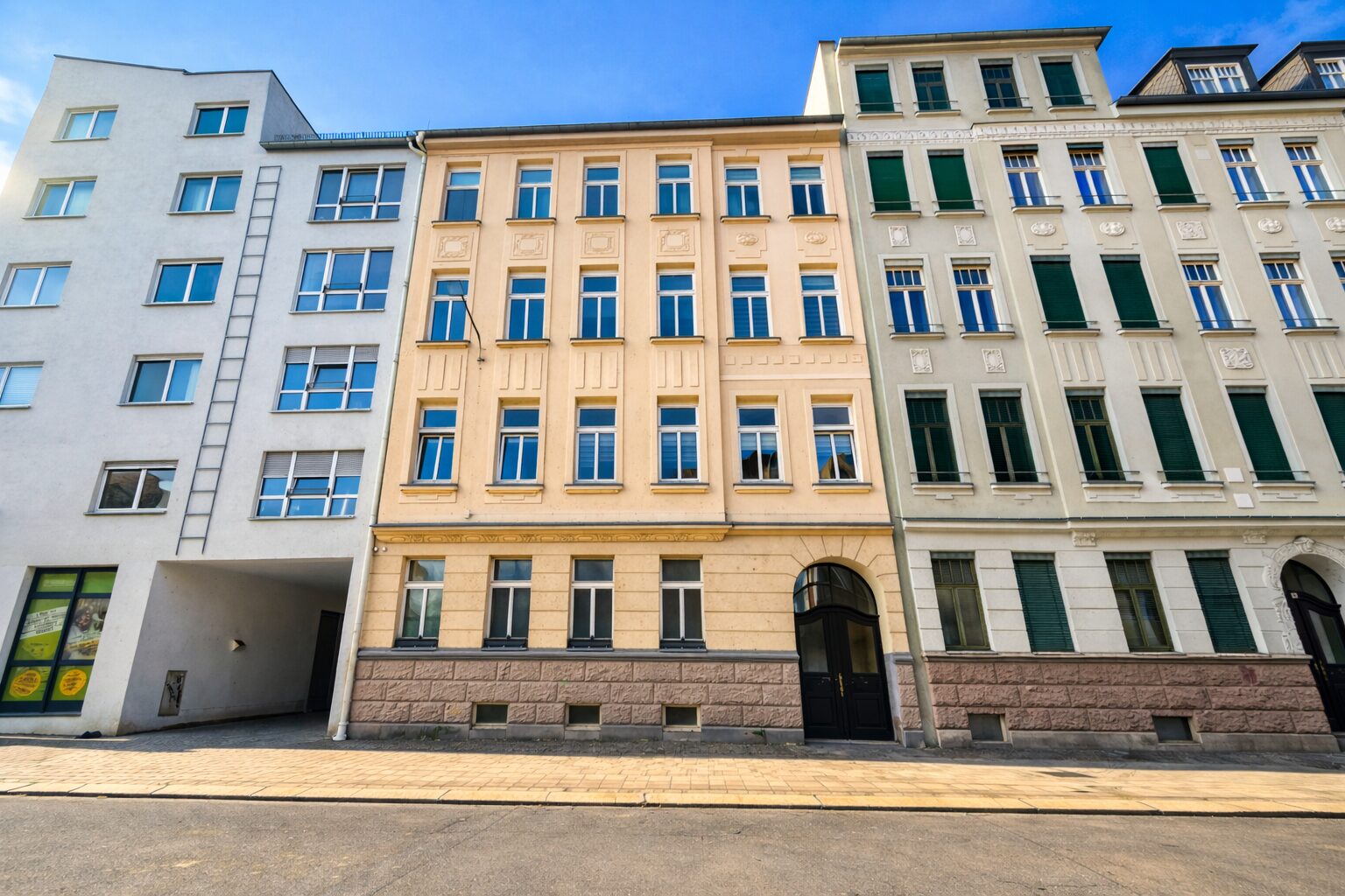 Row of pastel-colored, multi-story buildings with decorative facades along a sunny street and a dark arched doorway in the center building