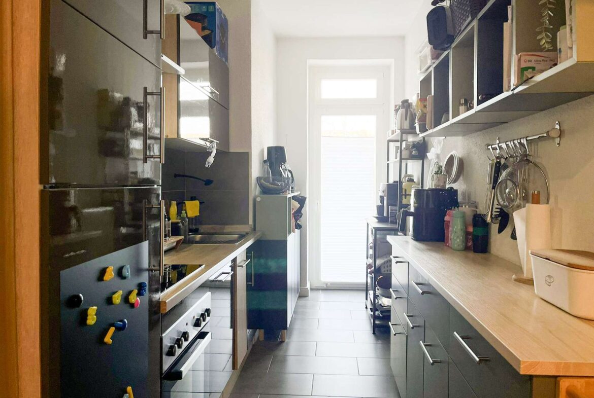 Narrow galley kitchen with dark glossy cabinets on both sides and a bright window at the far end.