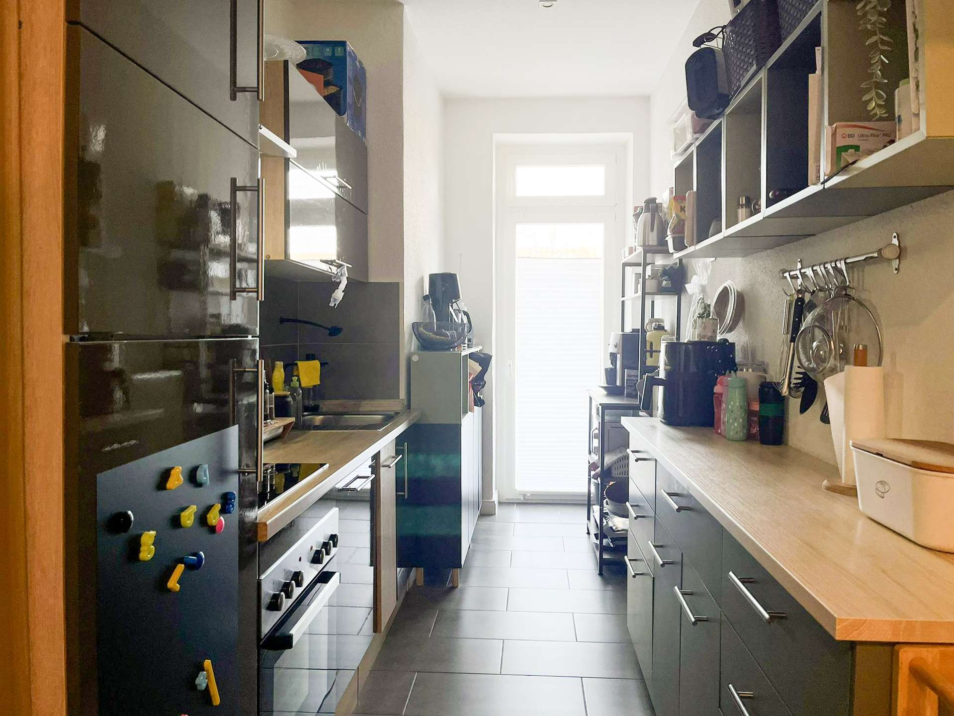Narrow galley kitchen with dark glossy cabinets on both sides and a bright window at the far end.