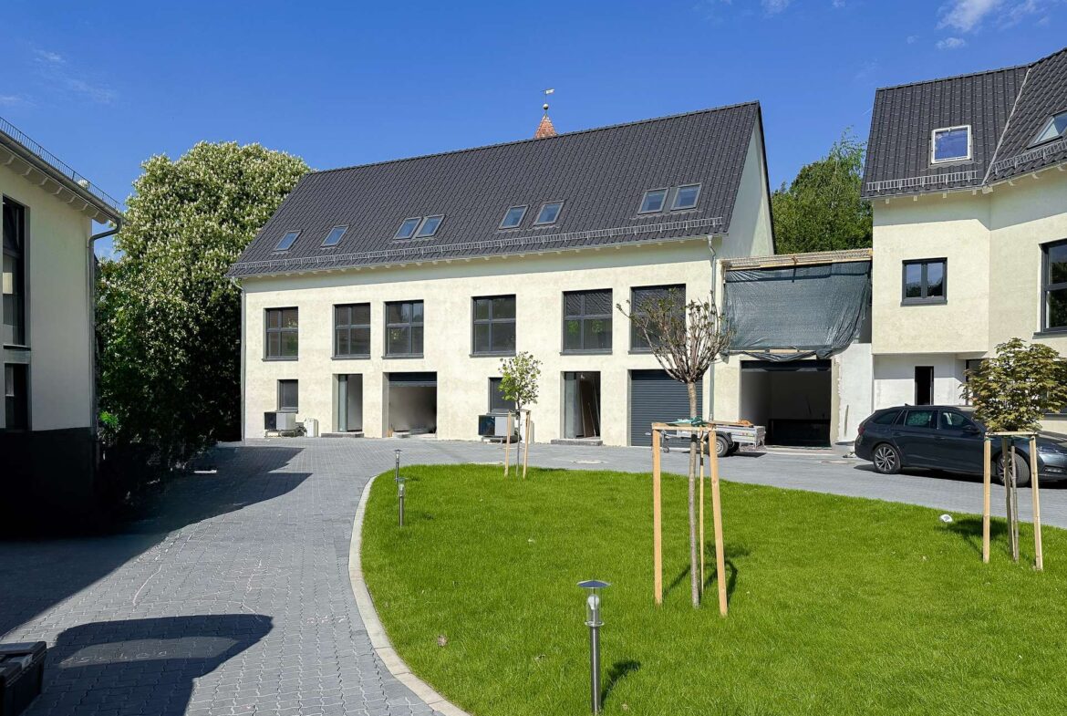 New residential buildings with dark metal roofs, multiple skylights, and a green lawn under a blue sky.