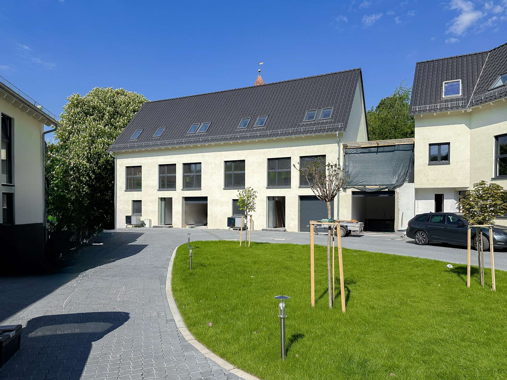 New residential buildings with dark metal roofs, multiple skylights, and a green lawn under a blue sky.
