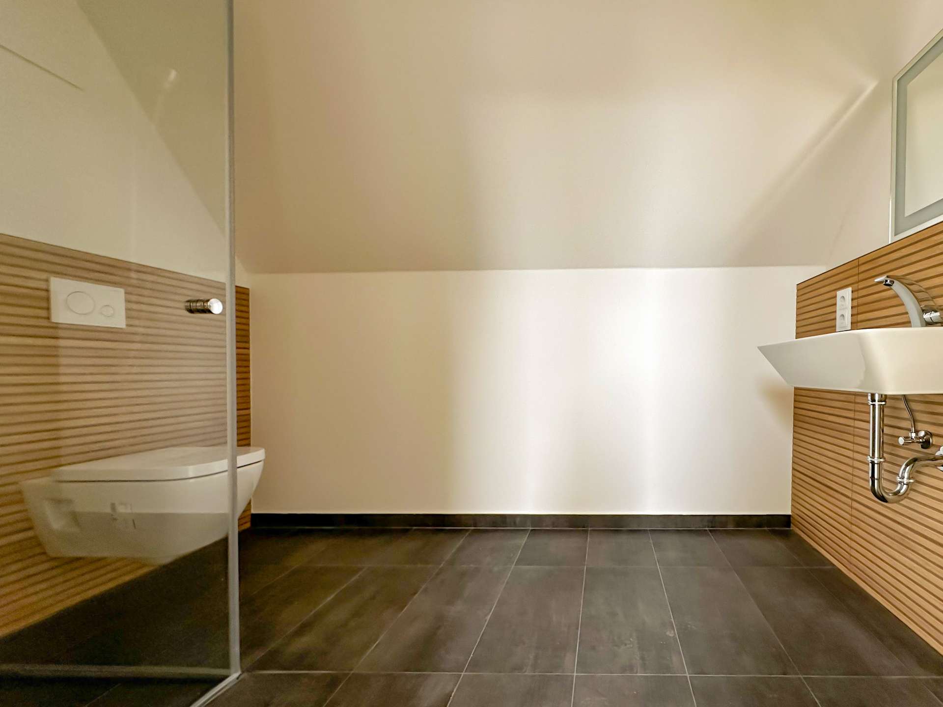 Modern bathroom with a wall-hung toilet beside a glass shower enclosure, wood-panelled walls, and a white sink with chrome fixtures on the right side.