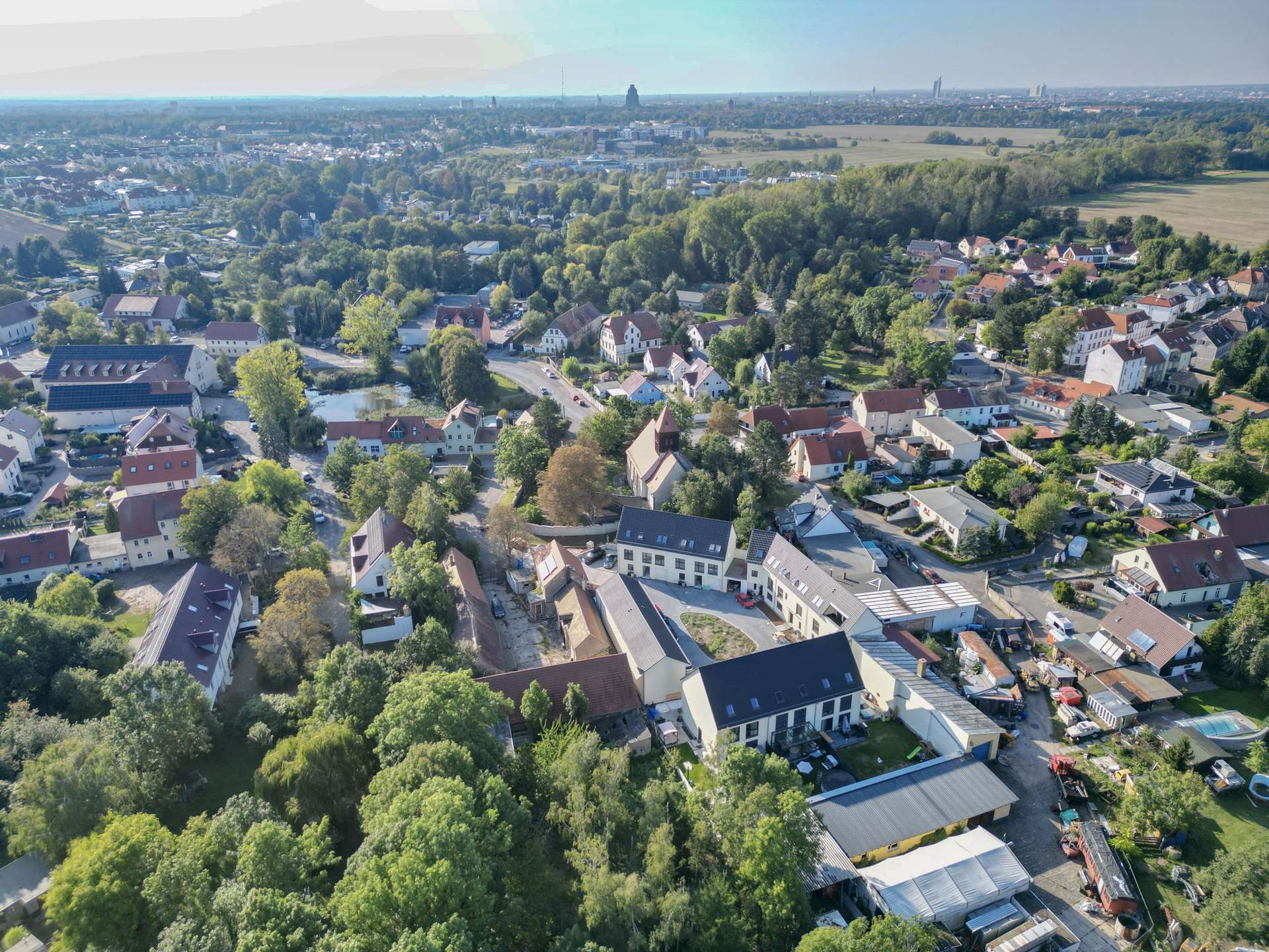Aerial view of a suburban town with red-roof houses, tree-lined streets, and fields in the distance.