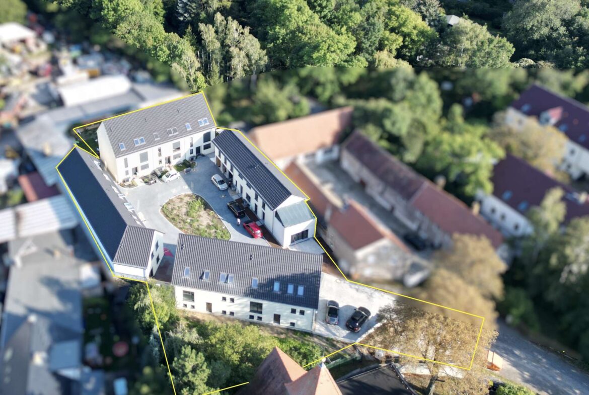 Aerial drone view of a multi-building residential complex with yellow boundary lines outlining the property, surrounded by trees and neighboring houses.