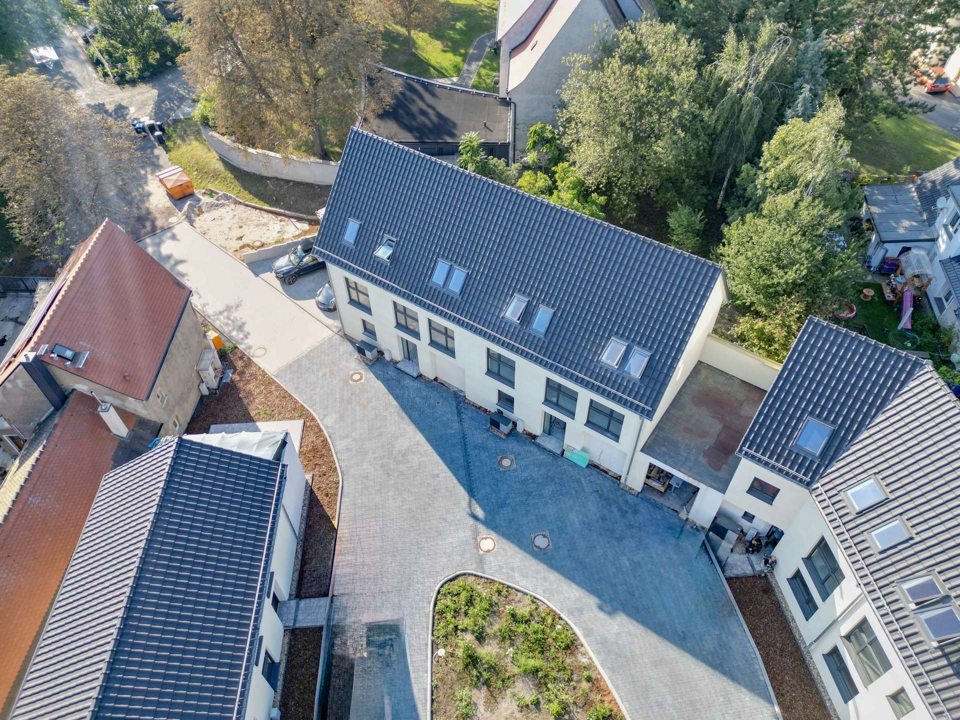 Aerial view of a residential complex with white buildings, blue-tiled roofs, and a central paved courtyard surrounded by trees.