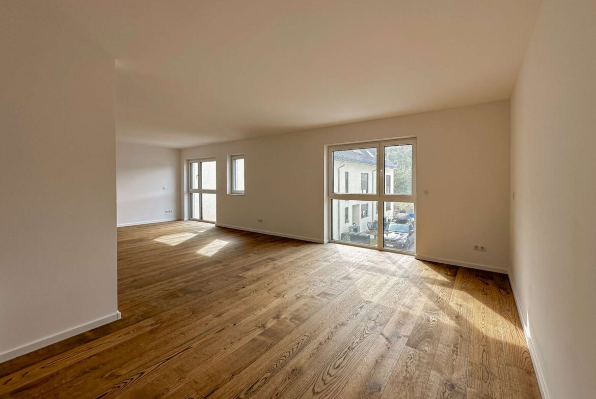 Bright, empty living room with warm wooden floors and large windows letting in natural light.