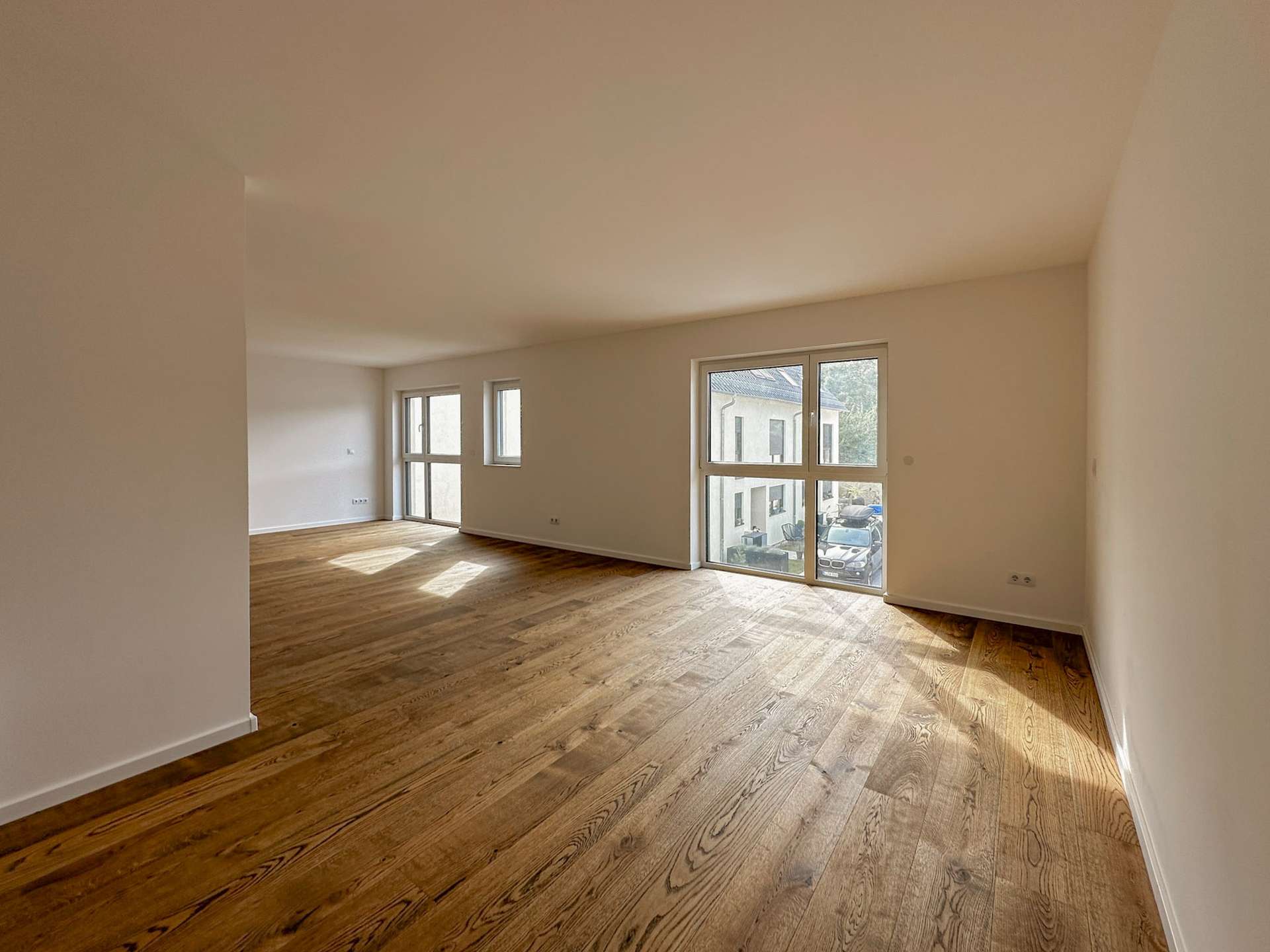 Bright, empty living room with warm wooden floors and large windows letting in natural light.