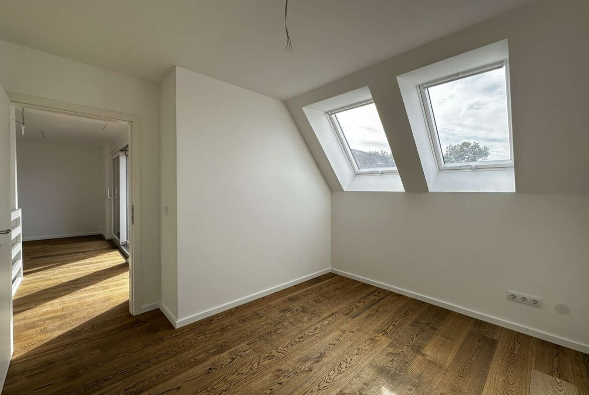 Empty attic-like room with a slanted ceiling, two rectangular skylights, and hardwood flooring