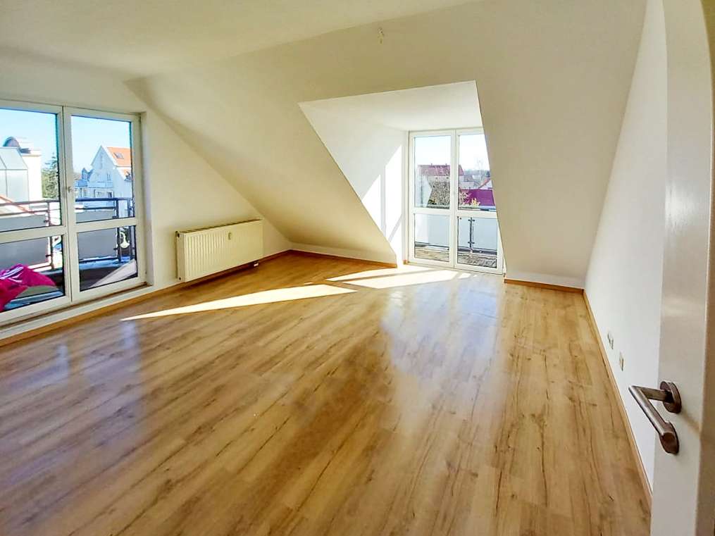 Bright empty attic room with light wood floor, slanted ceiling, and large glass doors to a balcony nearby.
