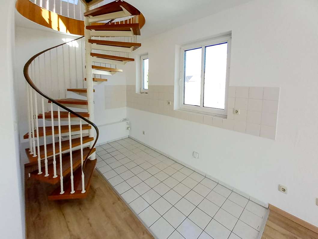 White-walled room with tiled floor and a wooden spiral staircase in the left corner, two windows along the back wall.