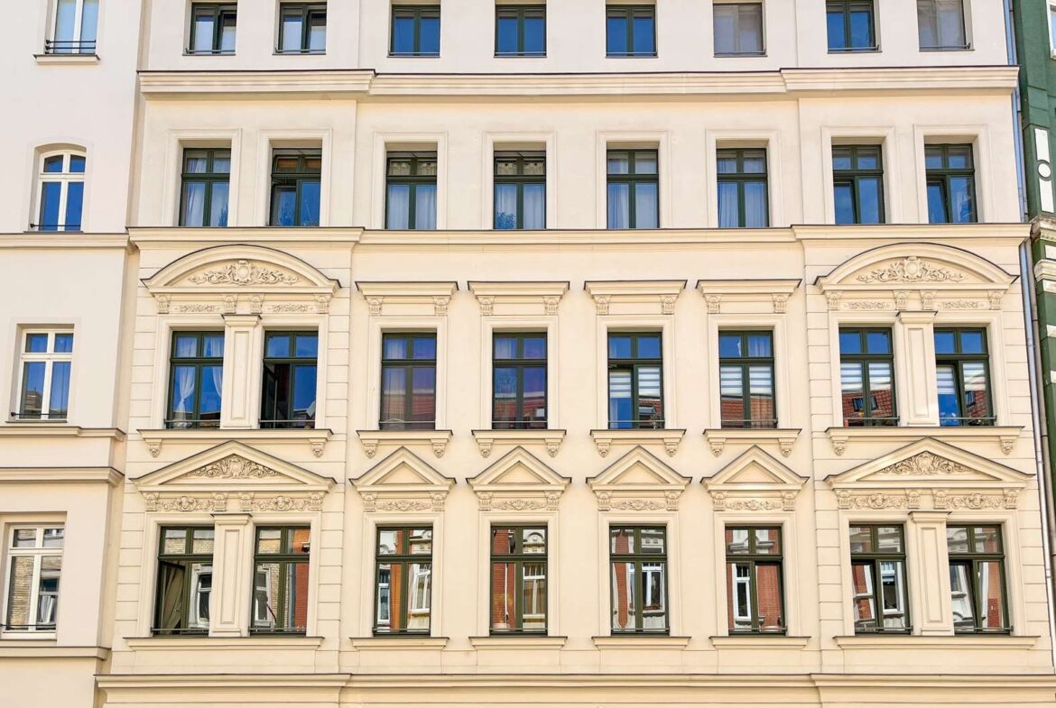 Historic cream-colored building facade with multiple aligned windows and decorative architectural details, including arched pediments and ornamented cornices.