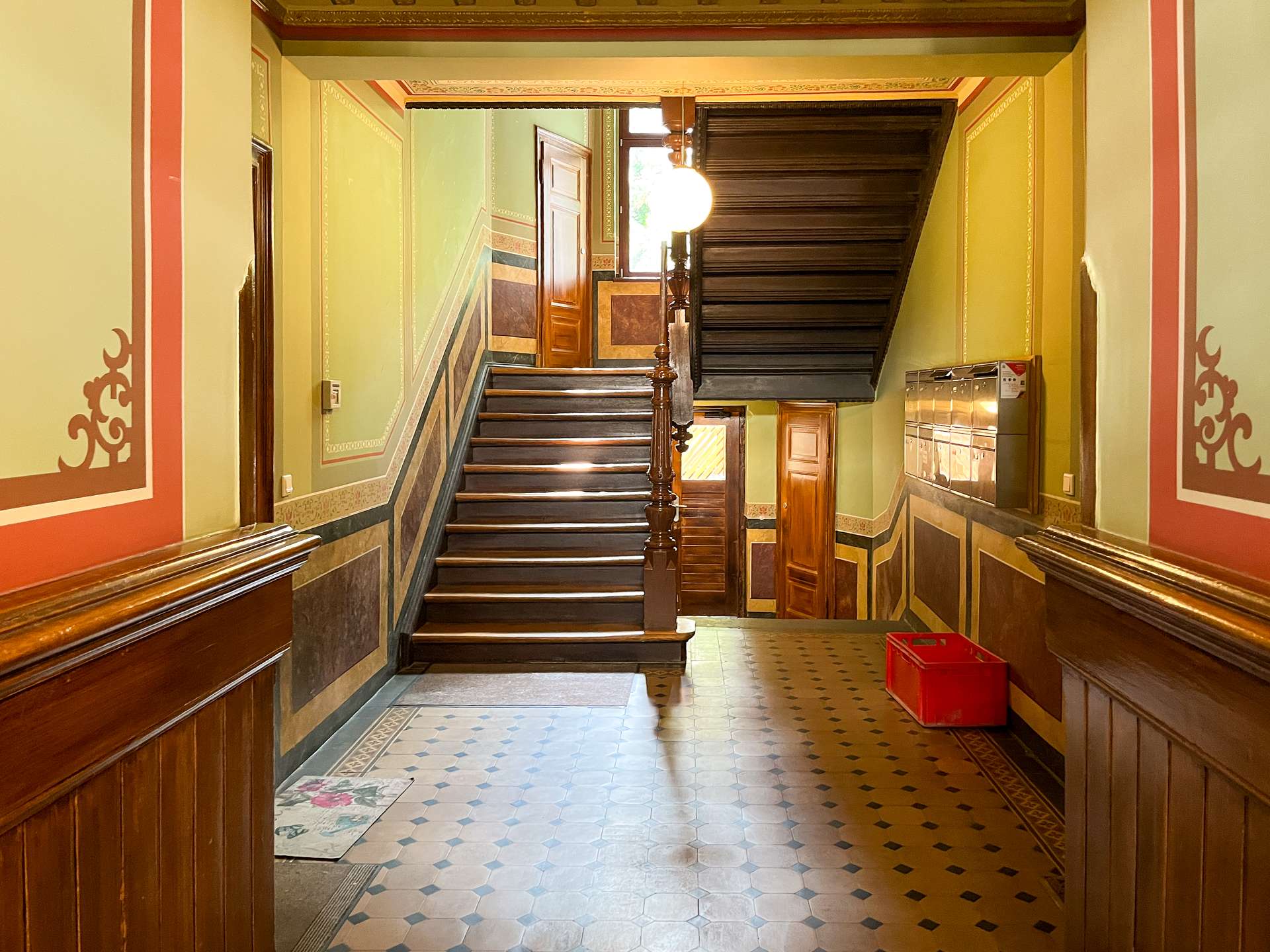 Interior staircase in a historic building: green walls with decorative trim, dark wooden banister, and a door at the landing.