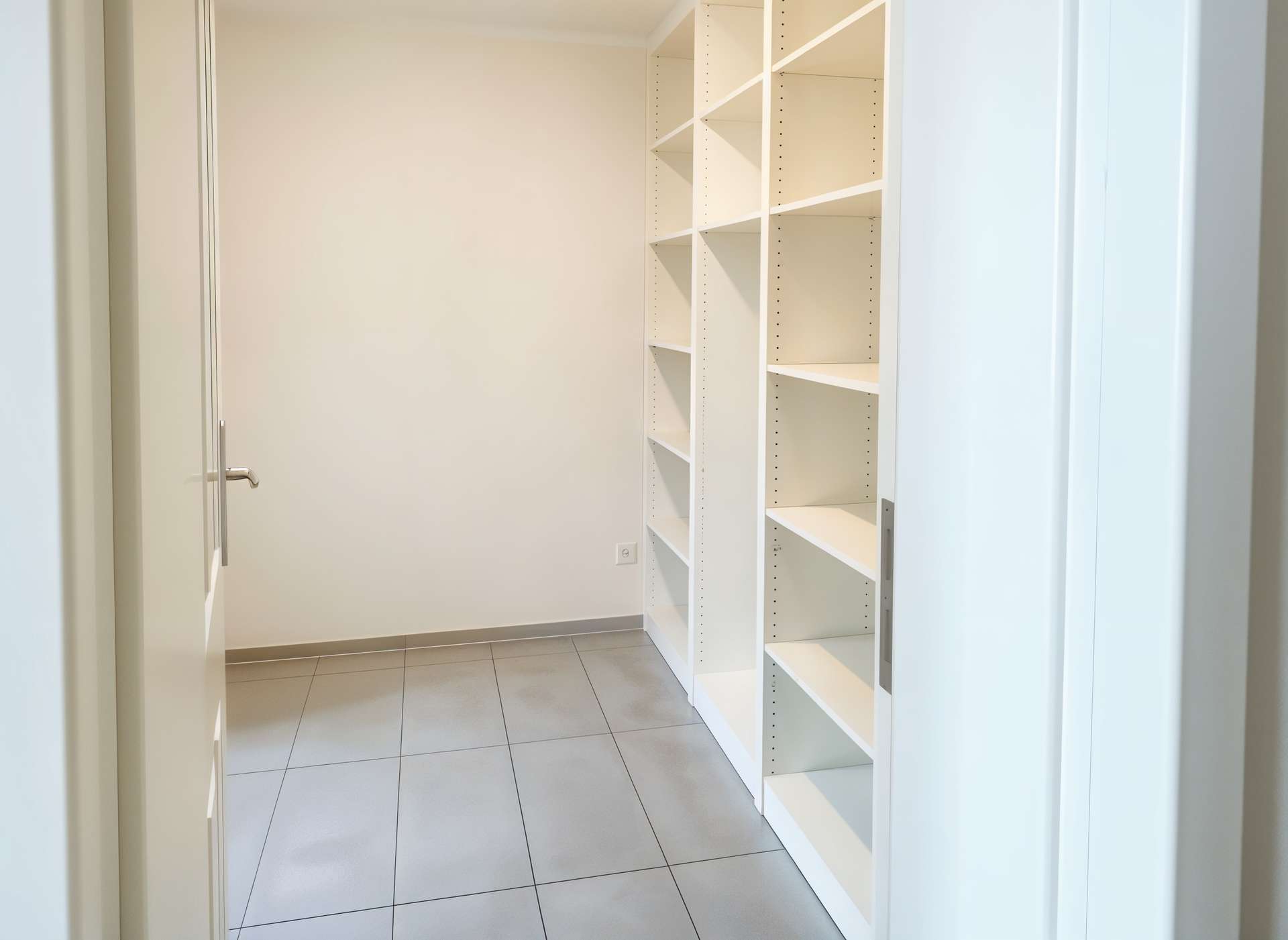 Tall white shelving unit with adjustable shelves along a beige wall in a narrow storage closet, empty and ready for use()