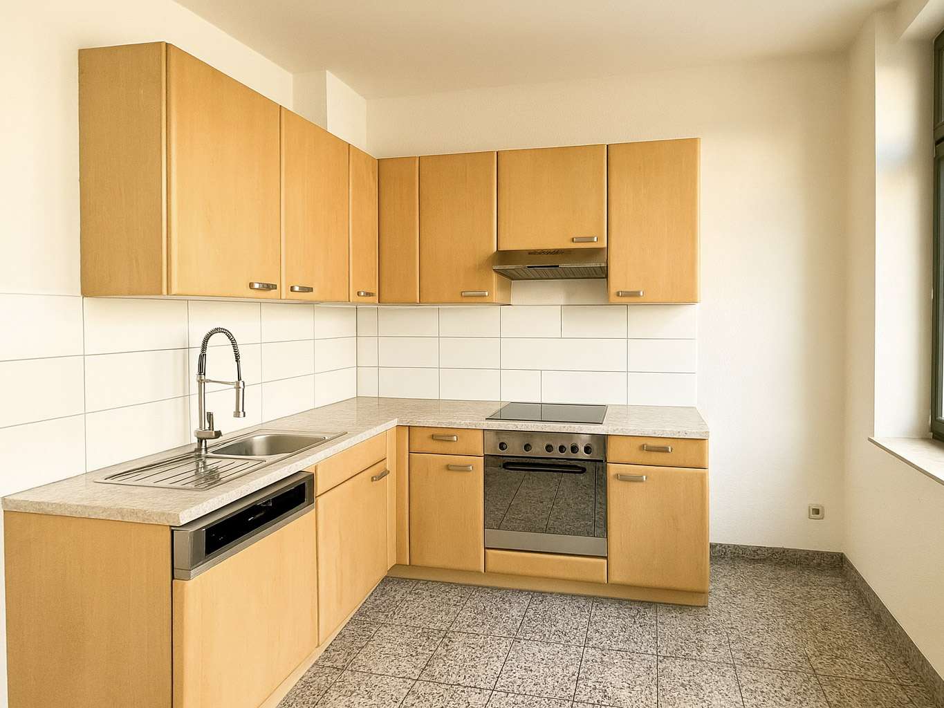 L-shaped kitchen with light wood cabinets, white tile backsplash, stainless steel sink, dishwasher, oven, and stovetop under a range hood. A window is on the right.