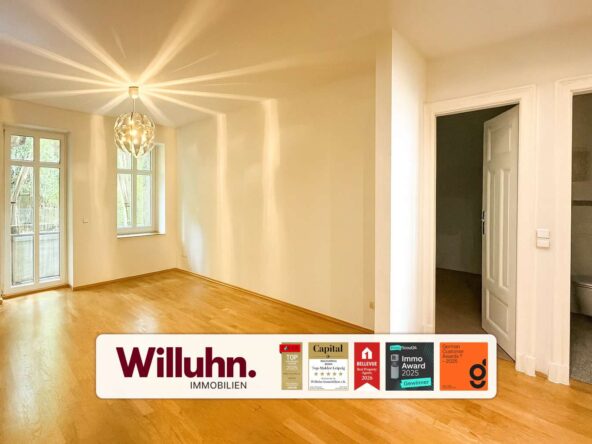 Bright empty living room with hardwood floor, large windows and a glass door to the outdoors; doorway to a bathroom on the right; pendant light overhead.