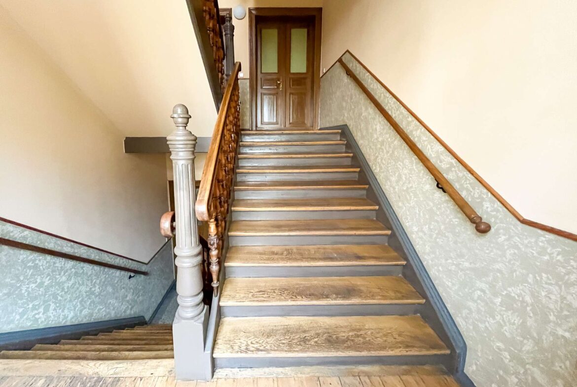 Wooden staircase with carved newel post leads up to a closed brown door at the landing, beige walls on both sides.