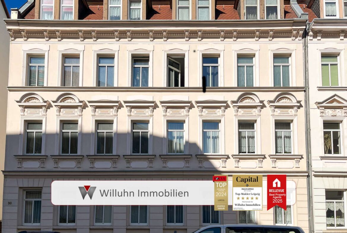 Facade of a cream-colored historic building with decorative windows and a white ground-floor storefront displaying real estate signs.