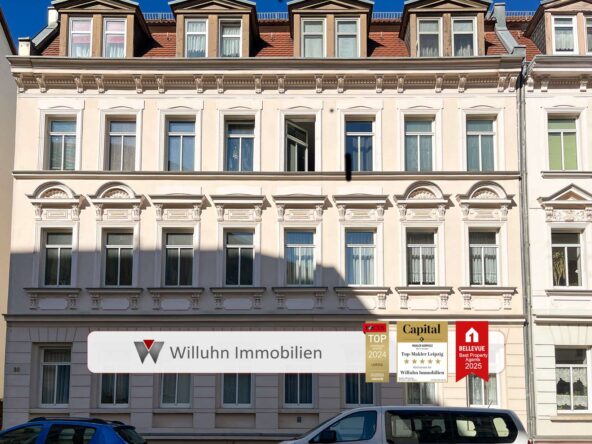 Facade of a cream-colored historic building with decorative windows and a white ground-floor storefront displaying real estate signs.