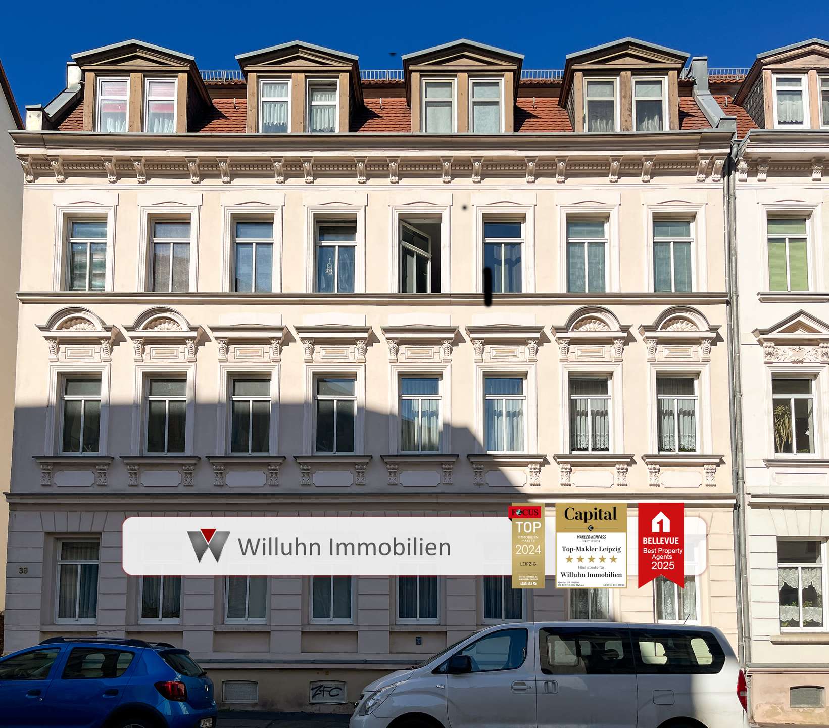 Facade of a cream-colored historic building with decorative windows and a white ground-floor storefront displaying real estate signs.