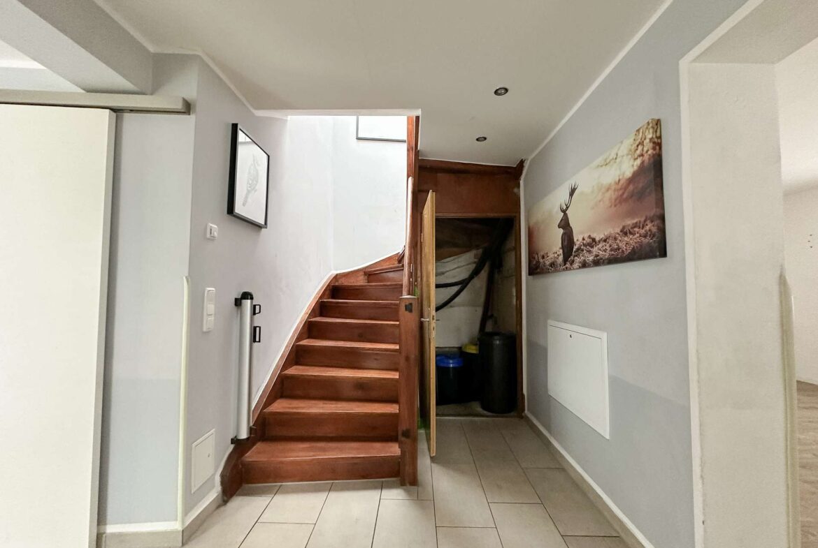 Interior hallway with a wooden staircase on the left, gray walls, and a large deer photo on the right wall; storage under the stairs.