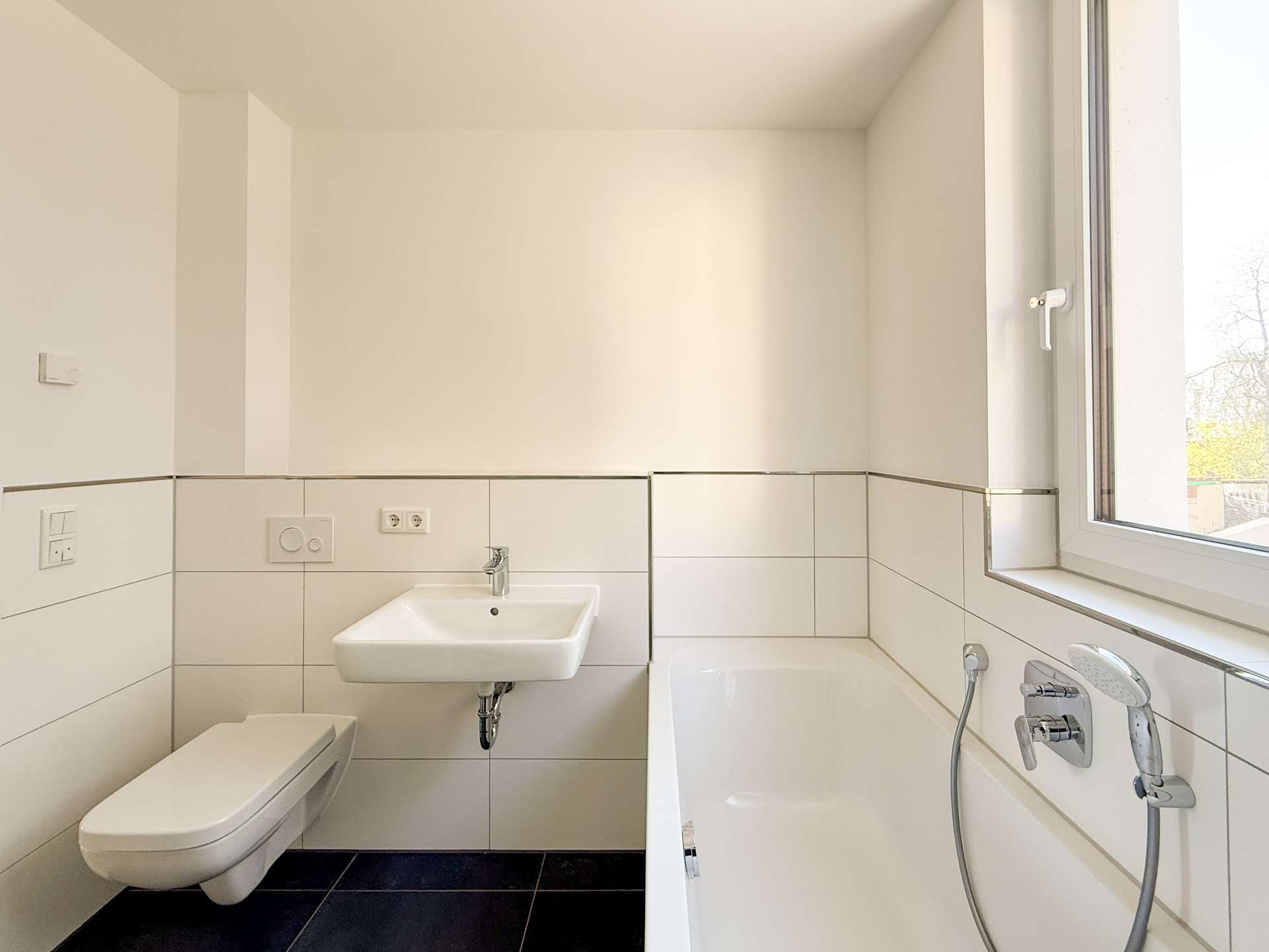 Modern bathroom with a wall-mounted toilet, small sink, and bathtub by a large window. (Informative)