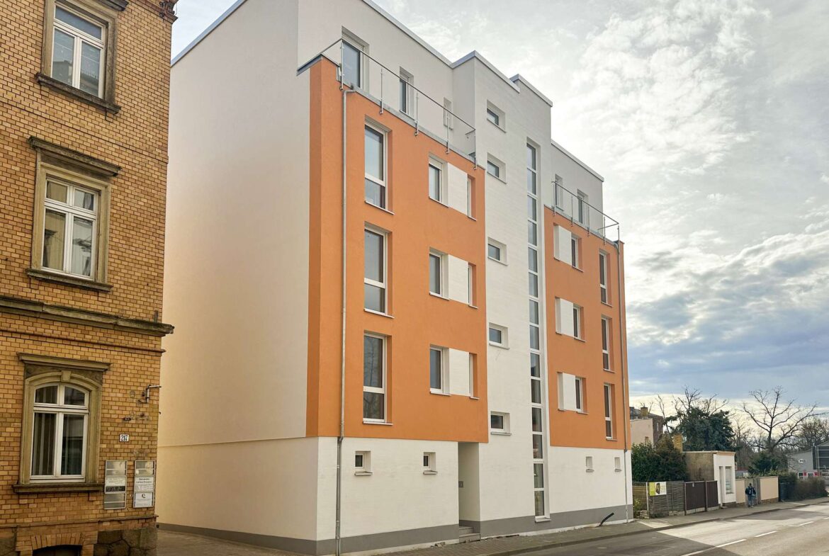 Brick building on the left beside a modern orange-and-white residential block on a city street.