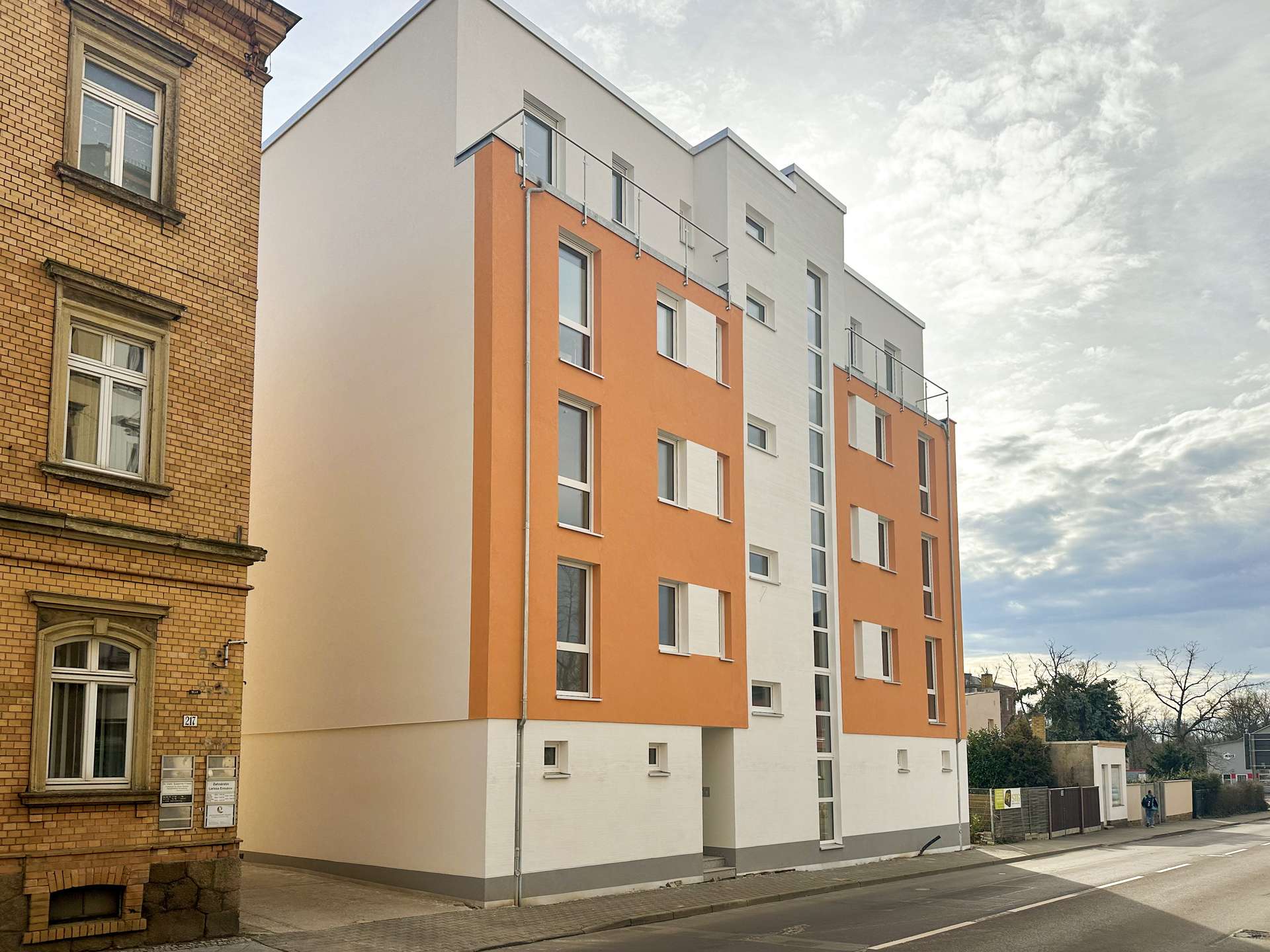 Brick building on the left beside a modern orange-and-white residential block on a city street.