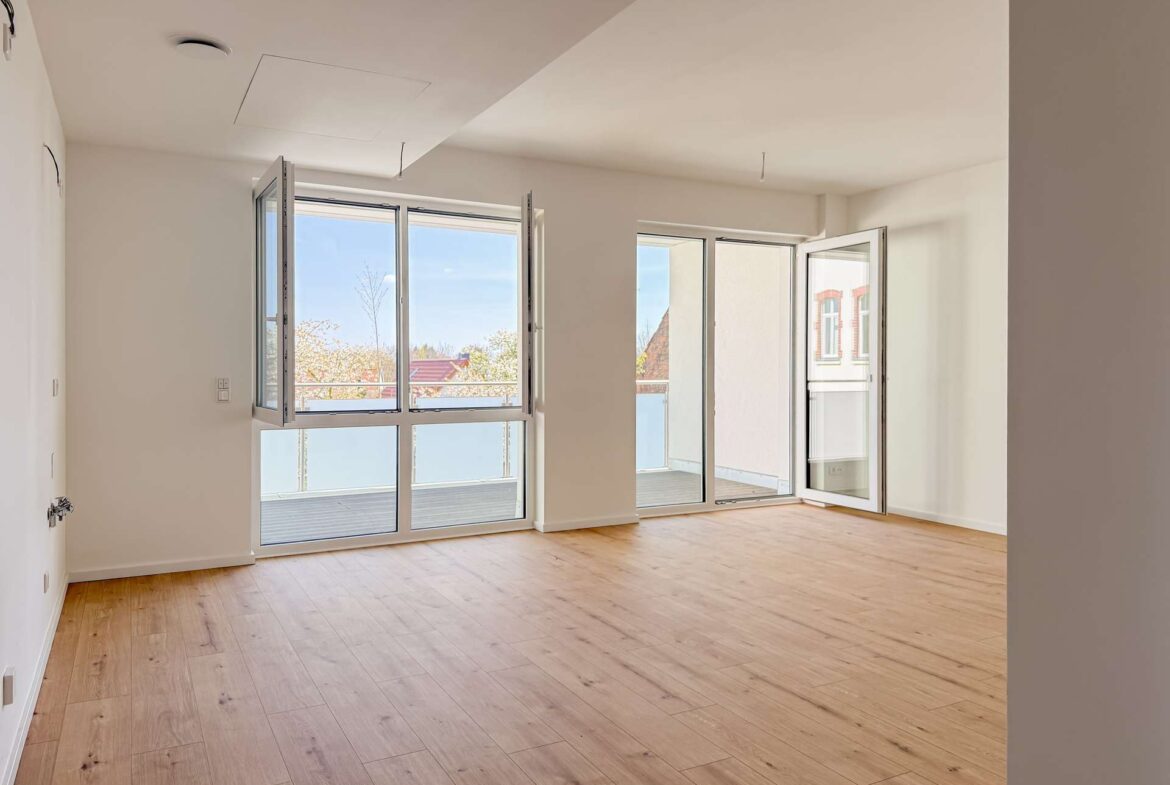 Bright, unfurnished living room with large glass doors opening to a balcony and light wood flooring.
