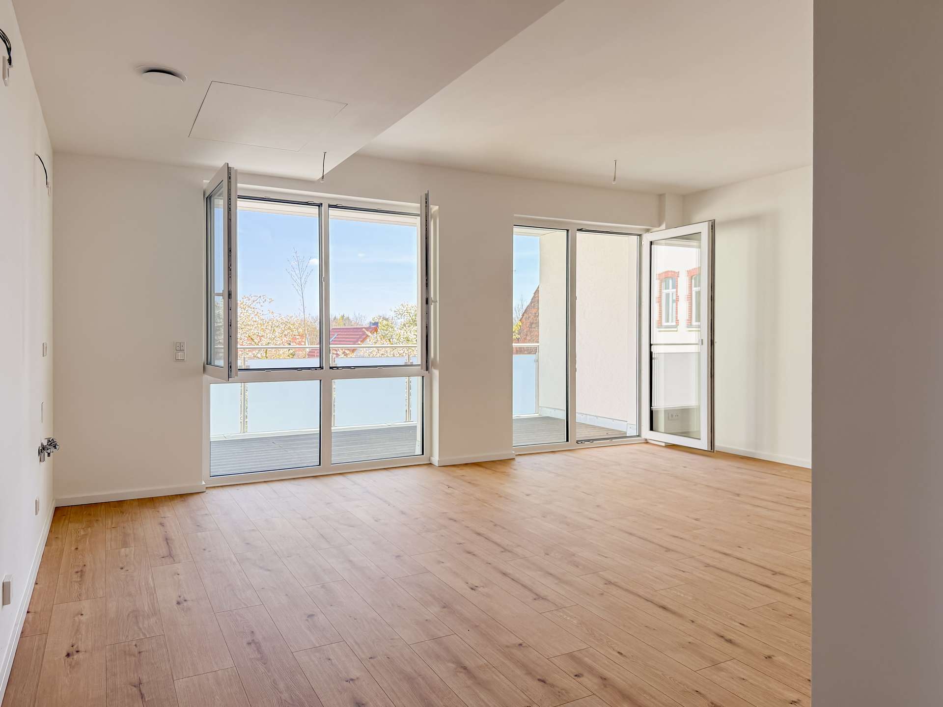 Bright, unfurnished living room with large glass doors opening to a balcony and light wood flooring.