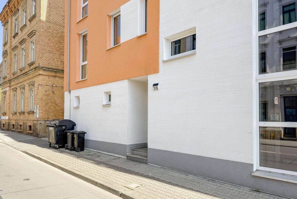 White and orange apartment building facade with a narrow entrance and small windows, on a paved sidewalk.