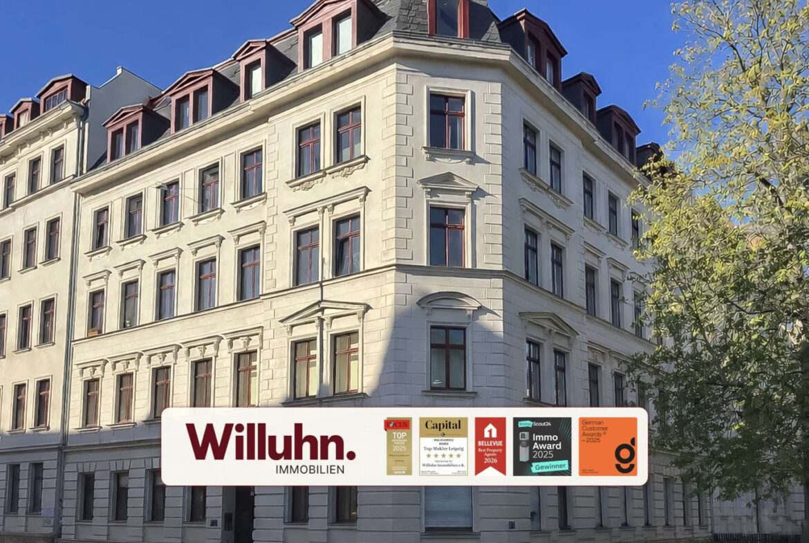 White multi-story building with red-framed windows under a blue sky; foreground shows a Willuhn Immobilien sign with award logos.
