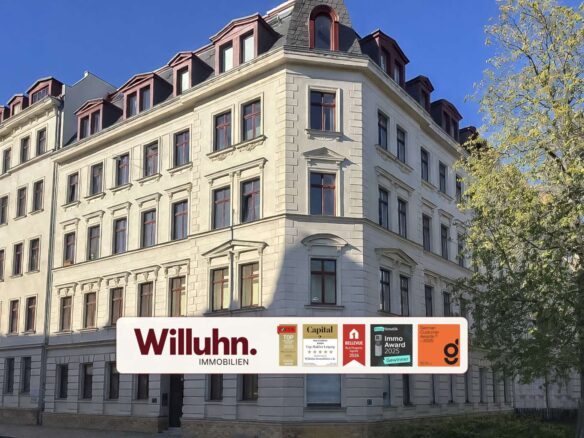 White multi-story building with red-framed windows under a blue sky; foreground shows a Willuhn Immobilien sign with award logos.