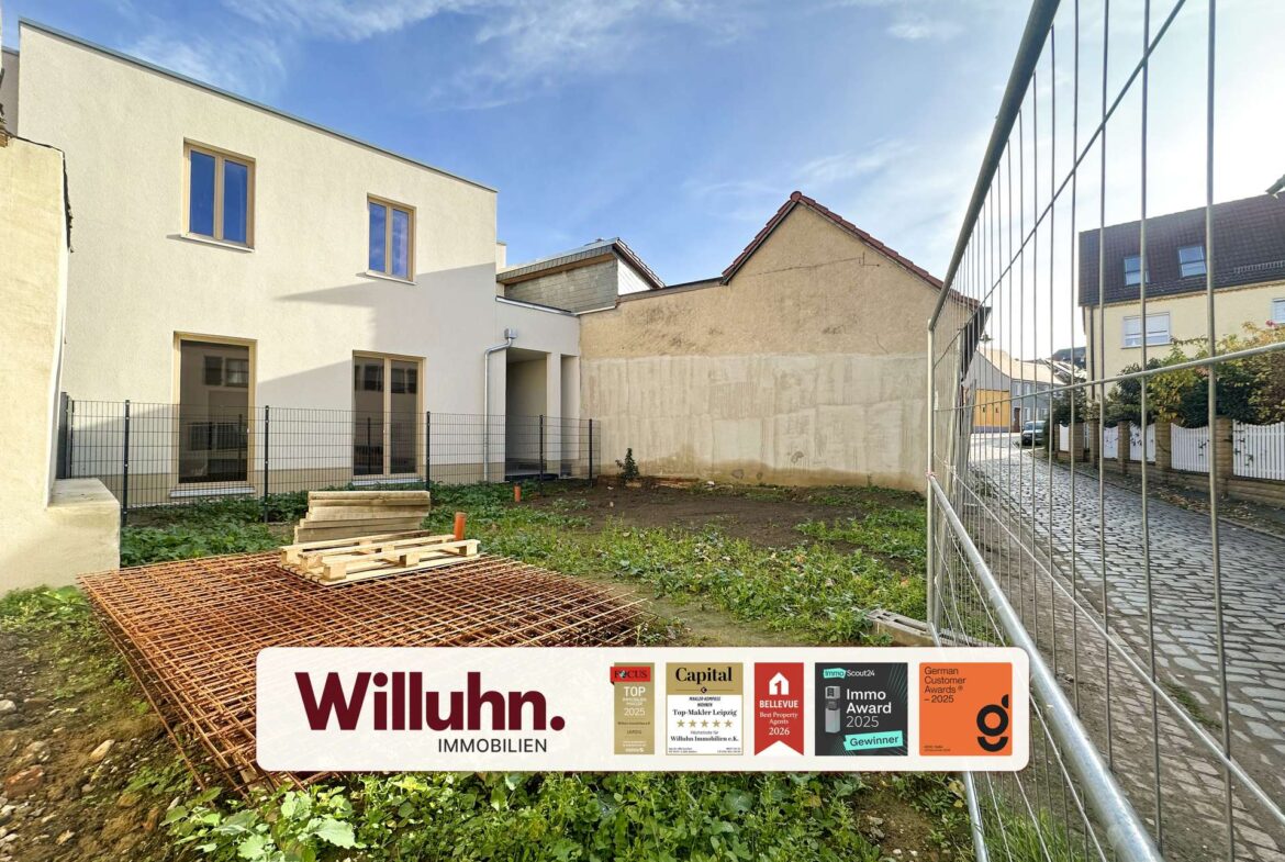 Construction site with a modern white building, metal fence, and a large Willuhn Immobilien sign showing awards.